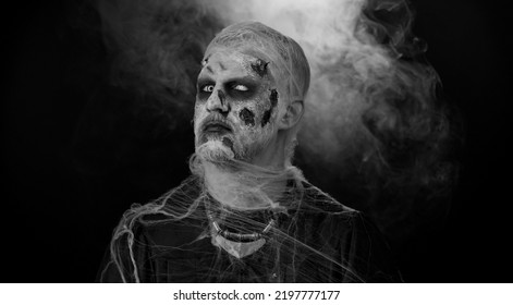 Sinister Man In Carnival Costume Of Halloween Crazy Zombie With Bloody Wounded Scars Face Screaming, Shouting, Trying To Scare On Black Room. Horror Theme Of Cosplay Wounded Undead, Beast, Monster