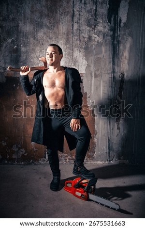 Sinister smiling man with a chainsaw and axe grins menacingly in a dark grunge abandoned room. Halloween theme