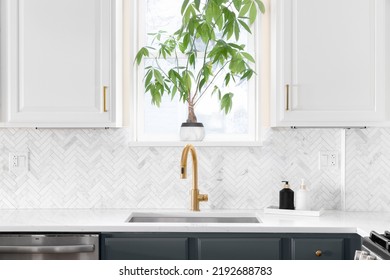 Sink Detail Shot In A Luxury Kitchen With Herringbone Backsplash Tiles. White Marble Countertop, And Gold Faucet.