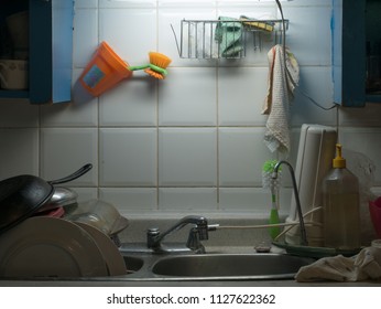 Sink In Dingy Kitchen, Full Drying Rack, Copy Space On Backsplash. Bits Of Dirt Visible. Translation On Brush Holder Text  