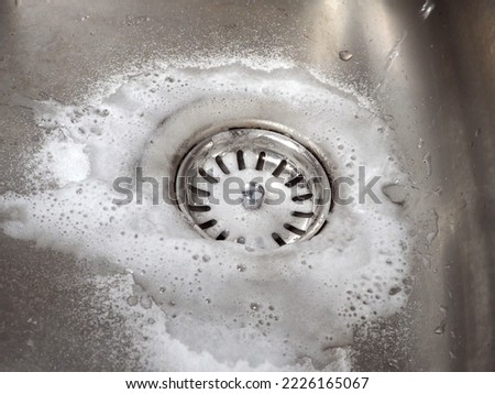 Sink drain cleaning process using baking soda and white vinegar. Close-up of a stainless steel kitchen sink. Tips for home eco-cleaning.