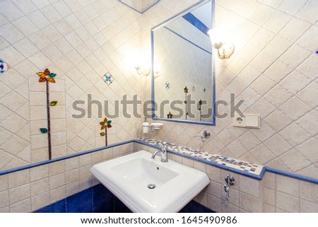 Sink and mirror in an expensive bathroom with white square tiles with uneven edges and a floral pattern.