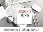 Sinking fund concept with notebook, keyboard, and magnifying glass on a gray office desk . 