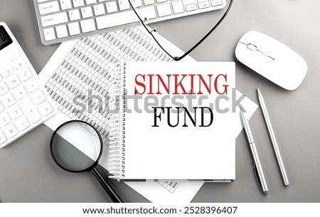 Sinking fund concept with notebook, keyboard, and magnifying glass on a gray office desk . 