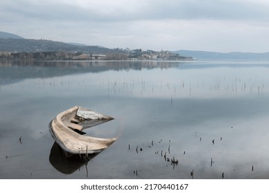 A Sinking Little Boat On Trasimeno Lake, Umbria, With Passignano Town In The Background