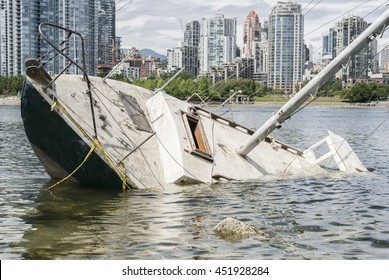 Sinking Sailboat Abandonned On The Shore Of A City
