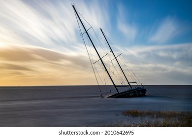 A Sinking Sailboat Close To Shore With Beautiful Wispy Clouds In The Background