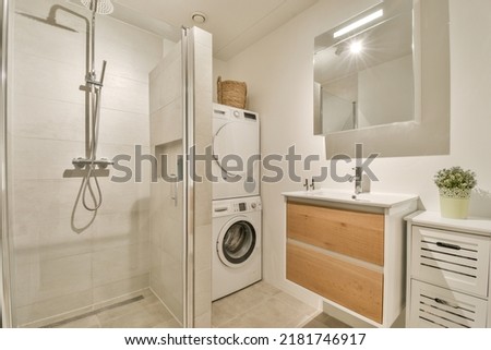 Sinks with mirrors and washing machine located near shower box with glass door in modern bathroom with white tiled walls