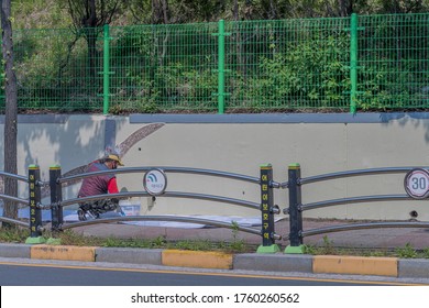 Sintanjin, South Korea; May 21,2020: Man Crouching On White Tarp Painting Wall Next To City Sidewalk.