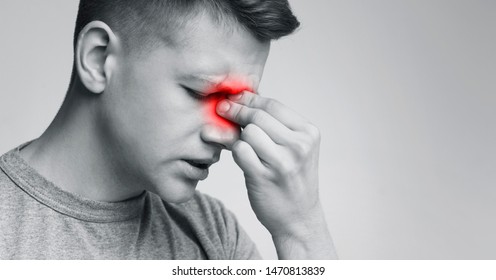 Sinus pain, sinusitis. Upset man holding his inflamed nose, black and white photo with red sore zone, panorama with free space
