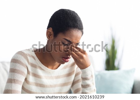 Sinusitis Concept. Sick Young Black Woman Touching Her Nose Bridge While Sitting On Couch At Home, African American Lady Feeling Unwell, Suffering From Rhinitis Or Seasonal Allergy, Free Space
