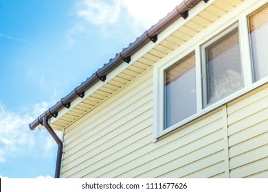 SIP Panel House Construction. Brown Rain Gutters. Drainage System With Plastic Siding And Eaves On Blue Sky Background.