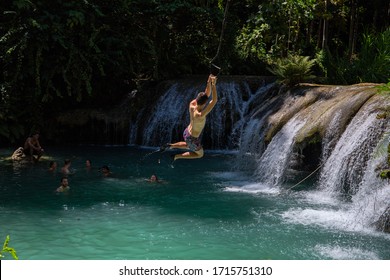 Siquijor, The Philippines - 12 Mar 2020: Boy Jumping With Tarzan Rope Over Waterfall. Rope Swing Jump Into Waterfall. South Asia Ecotourism And Adventure. Young Traveler On Gap Year. Extreme Sport