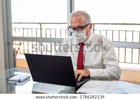 Sir typing on the notebook, working on the home office system in times of pandemic by the Corona virus. Sir works at home wearing a shirt and tie and wearing a mask