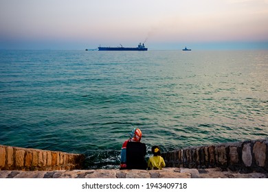 Siraf, Iran, March 2021: A Mother And Her Daughter Are Watching An Oil Tanker Ship. The Sharp Decline In Oil Exports Due To US Sanctions Has Increased Economic Problems For The Iranian People.