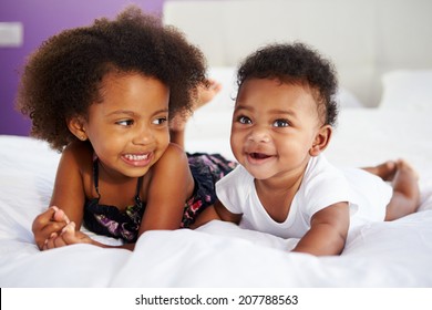 Sister With Baby Brother Lying On Parent's Bed