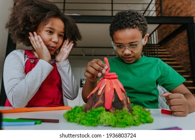 Sister and brother having fun making DIY volcano model from kids play clay for school project. Home education concept.
