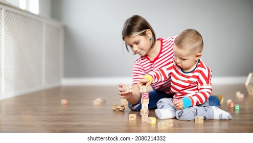 Sister and brother playing with cubes together on the floor indoors. - Shutterstock ID 2080214332