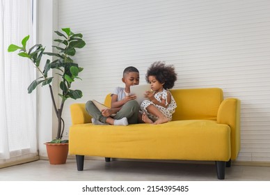 Sister and brother playing togetherness fun in living room, Two little kids siblings seated on sofa using tablet smartphone and book - Powered by Shutterstock