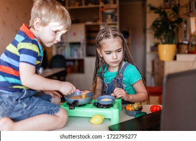 Sister And Brother Watching Video On The Screen Of Laptop And Playing In Master Chef, Preparing Dinner With Toy Vegetables And Real Fresh Eggs, Online Cooking During Lockdown, At-home Kid Activity