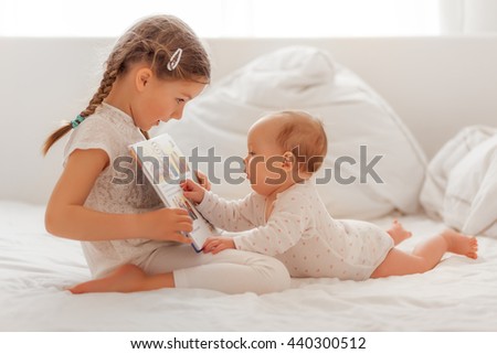 sister explaining and reading baby in bed a book