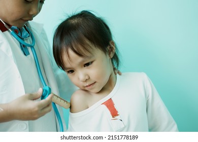 ฺBrother and sister are playing doctor and hospital using toy wooden syringe  and medical uniform at home. Soft focus.