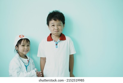 ฺBrother and sister are playing doctor and hospital using thermometer toy and medical uniform at home. Soft focus.