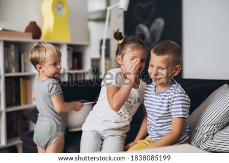 sister whispering to her brother, other brother looking, at home