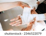 Sister wrapping her brother wrist and arm with bandage around injured hand at home. First aid, accident and injury treatment concept. Closeup