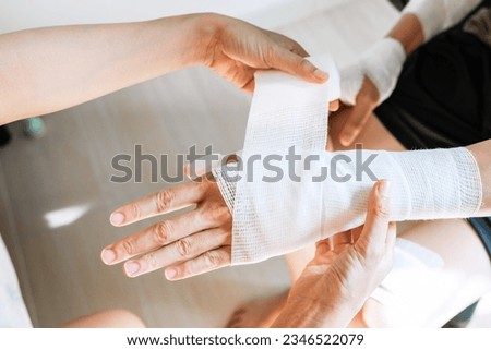 Sister wrapping her brother wrist and arm with bandage around injured hand at home. First aid, accident and injury treatment concept. Closeup