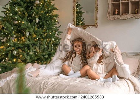 Sisters play in their parents' bed hiding under the covers. Christmas happy children's morning