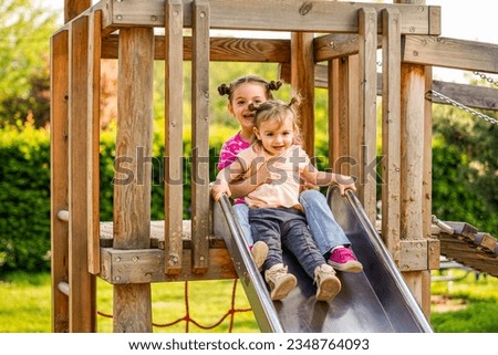 Sisters slide together in a playground - Children have fun together
