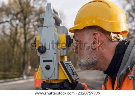 Site engineer operating his instrument during roadworks. Builder using total positioning station tachymeter on construction site for new road setting out