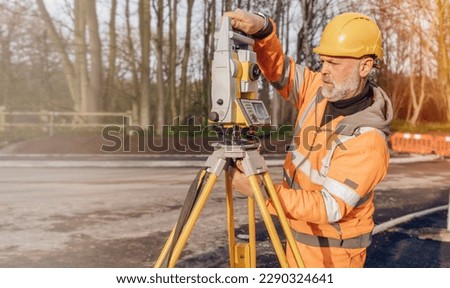 Site engineer operating his touch screen controller instrument during roadworks. Builder using touch screen controller to control total positioning station tacheometer on construction site   