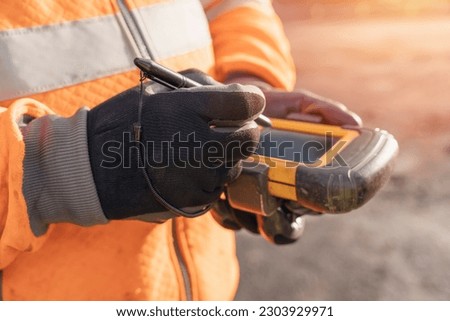 Site engineer operating his touch screen controller instrument during roadworks. Builder using touch screen controller to control total positioning station tachymeter on construction site  