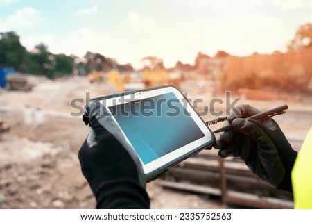 Site engineer surveyor using rugged tablet controller computer to operate EDM total station for setting out and surveying close-up