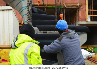 Site manager checks with a spirit level whether the concrete stairs are level to be lifted by the construction crane to lower over the wall to the ground floor apartment building                     