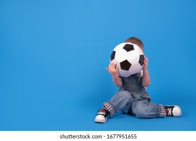 Сhild sits with a ball on a blue background, holding a soccer ball in front of him. Football competition. Sport concept of football, World Cup or European football tournament. - Shutterstock ID 1677951655