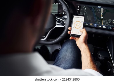 Sits in the car. Close up view of man's hand that holds phone with labels and icons. Conception of remote control.