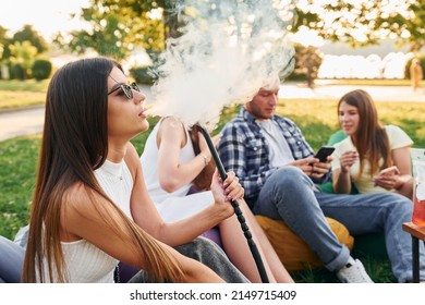 Sitting In The Armchair Bags And Smoking Hookah. Group Of Young People Have A Party In The Park At Summer Daytime.