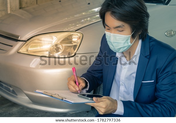 Sitting Asian Insurance Agent or Insurance\
Agency in Suit Wear Mask Checking Car Crash Data Report from\
Accident for Claim at Garage in Vintage\
Tone