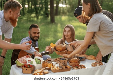 Sitting by the table. Group of friends are having picnic on the field with food in eco boxes. - Powered by Shutterstock