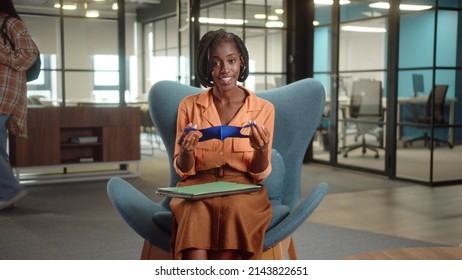 Sitting In The Entrance Hall In The University, A Young African Professor Is Talking About The Importance Of Wearing A Protective Mask And Putting It On Her Face