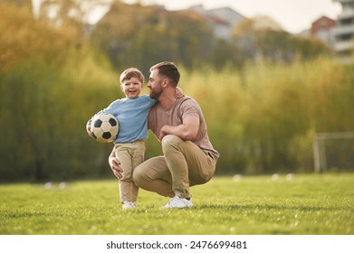 Sitting, holding soccer ball. Happy father with son are having fun on the field at summertime. - Powered by Shutterstock