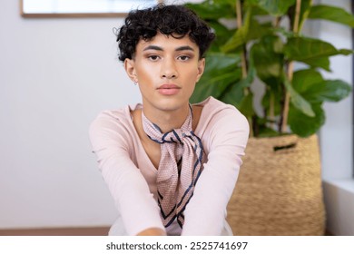 Sitting indoors, transgender transgender woman posing confidently with plant in background. LGBT, self-expression, identity, houseplant, inclusivity, diversity - Powered by Shutterstock