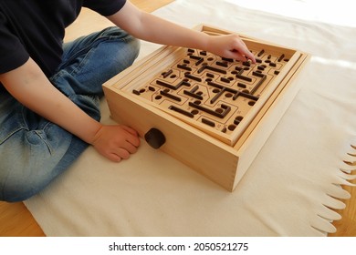 Sitting kid playing with a labyrinth maze game. Wooden toy, old style with a metal ball. No face. Stockholm, Sweden.
