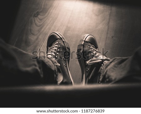 Sitting and looking at two legs with retro sneakers and jeans, wooden floor, moody light and shadows, first-person perspective, vintage look