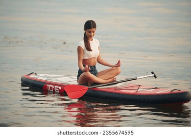 Sitting in lotus pose. Young woman is on sup boards in the lake. - Powered by Shutterstock