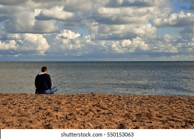 Sitting man doing yoga on shore of ocean