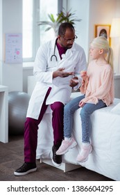 Sitting Near Doctor. Blonde-haired Stylish Girl Wearing Jeans And Pink Blouse Sitting Near Doctor